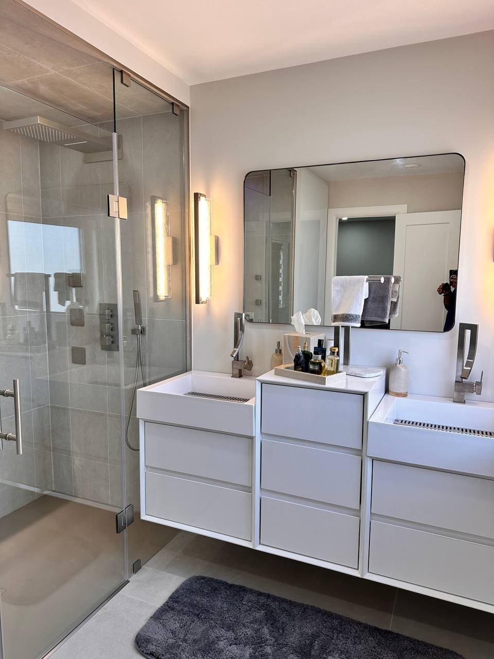 Renovated bathroom with a glass shower enclosure, twin white vanities and a full width mirror