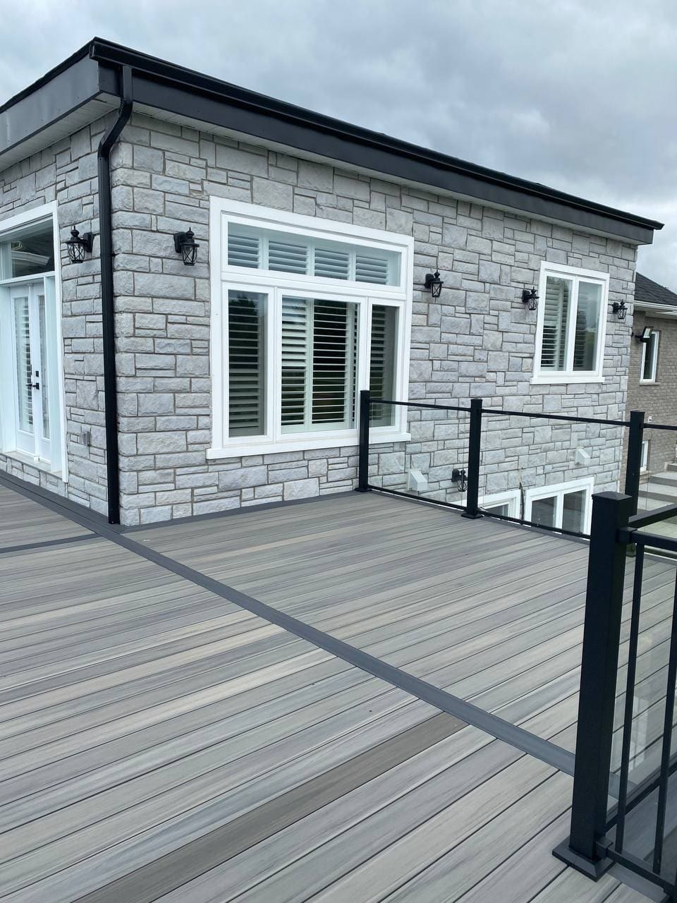 Rear addition with stone cladding, a composite deck and a glass panel railing