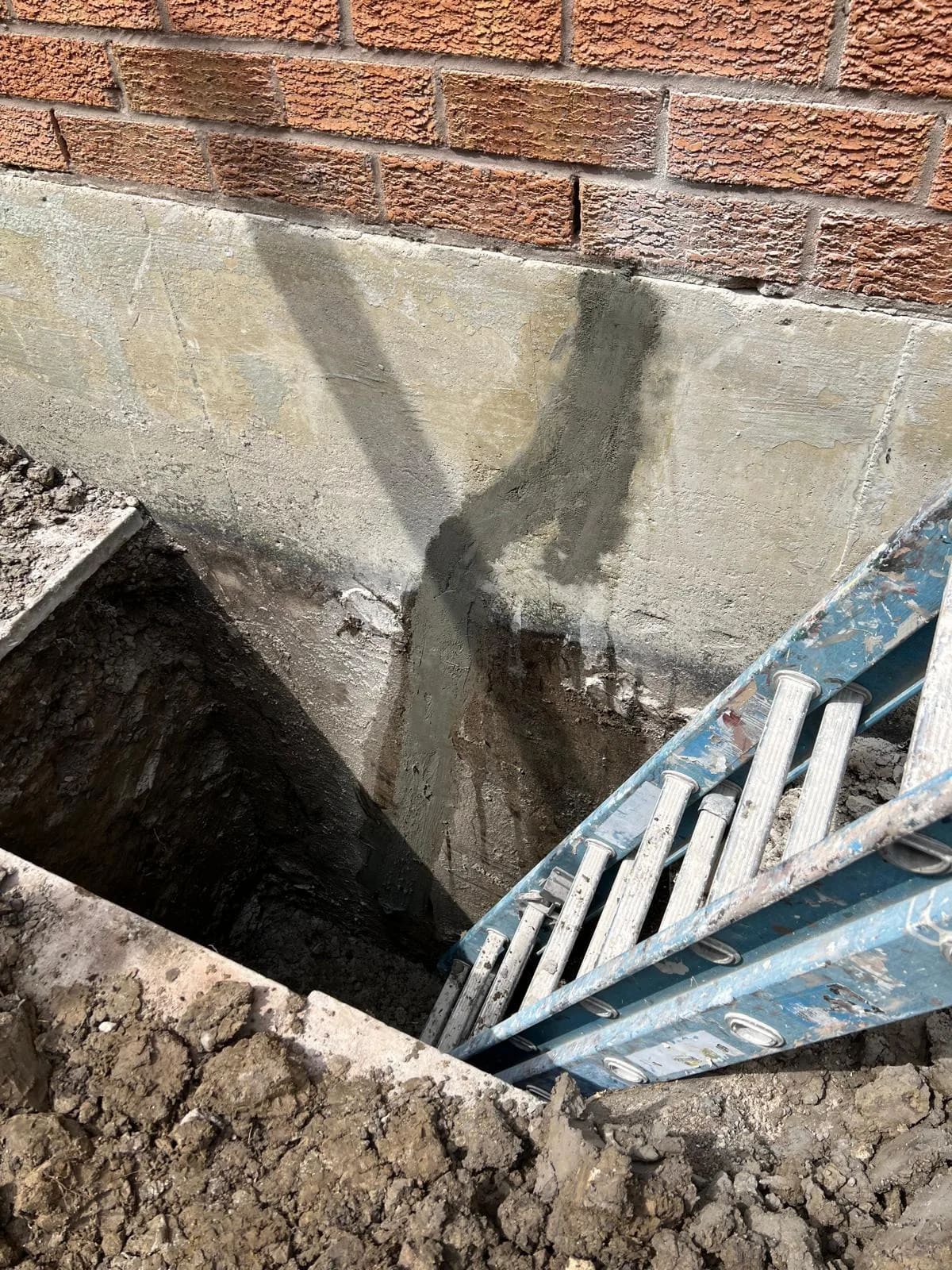 Foundation excavation beside the house exposing the concrete foundation wall during waterproofing and repair work.